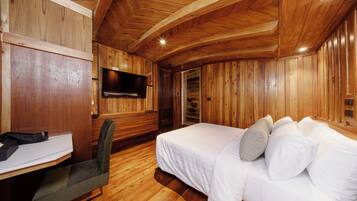A wooden-paneled room with a bed, a desk, and a television.