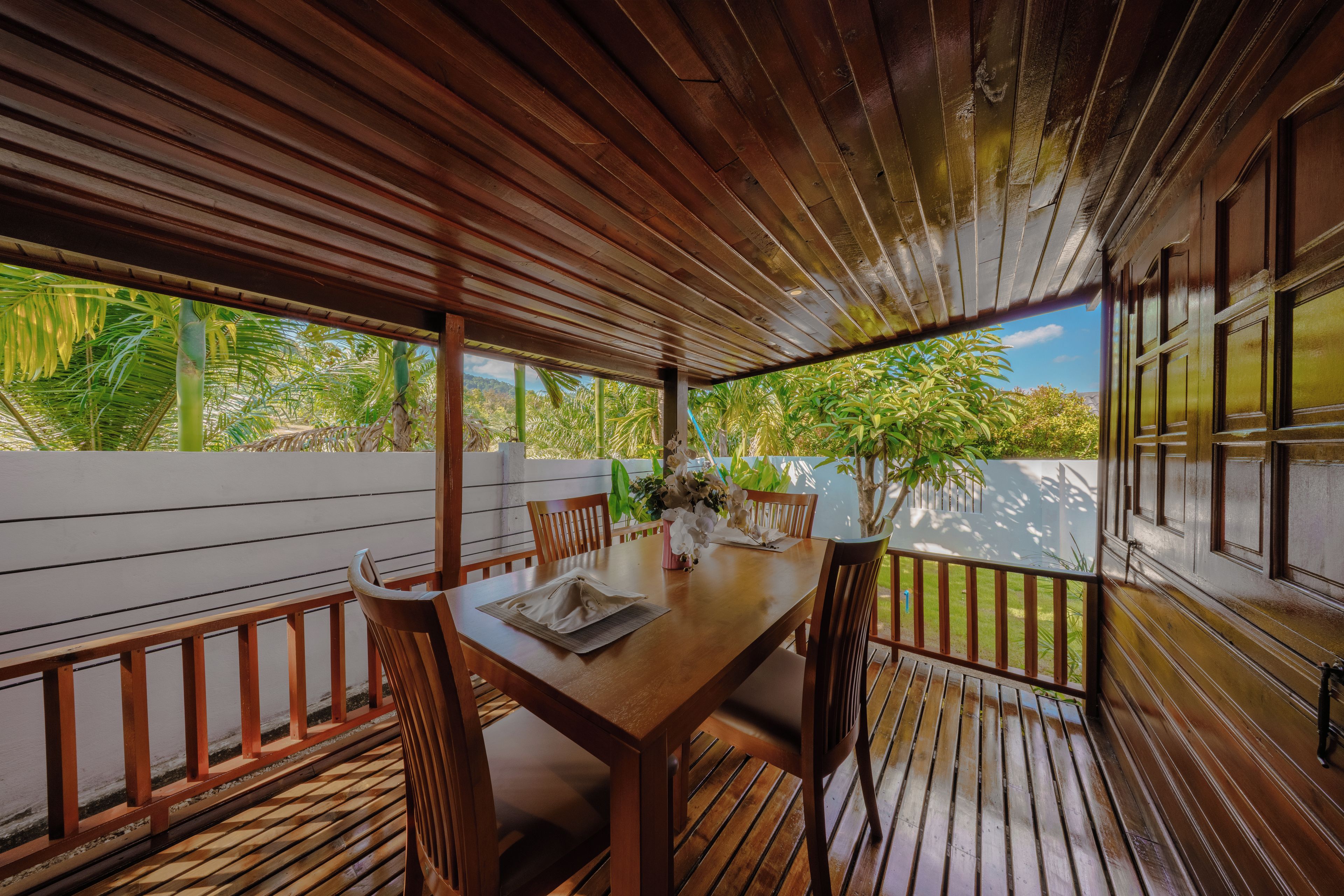 A wooden deck with a table set for dining, surrounded by chairs, and a view of tropical vegetation.