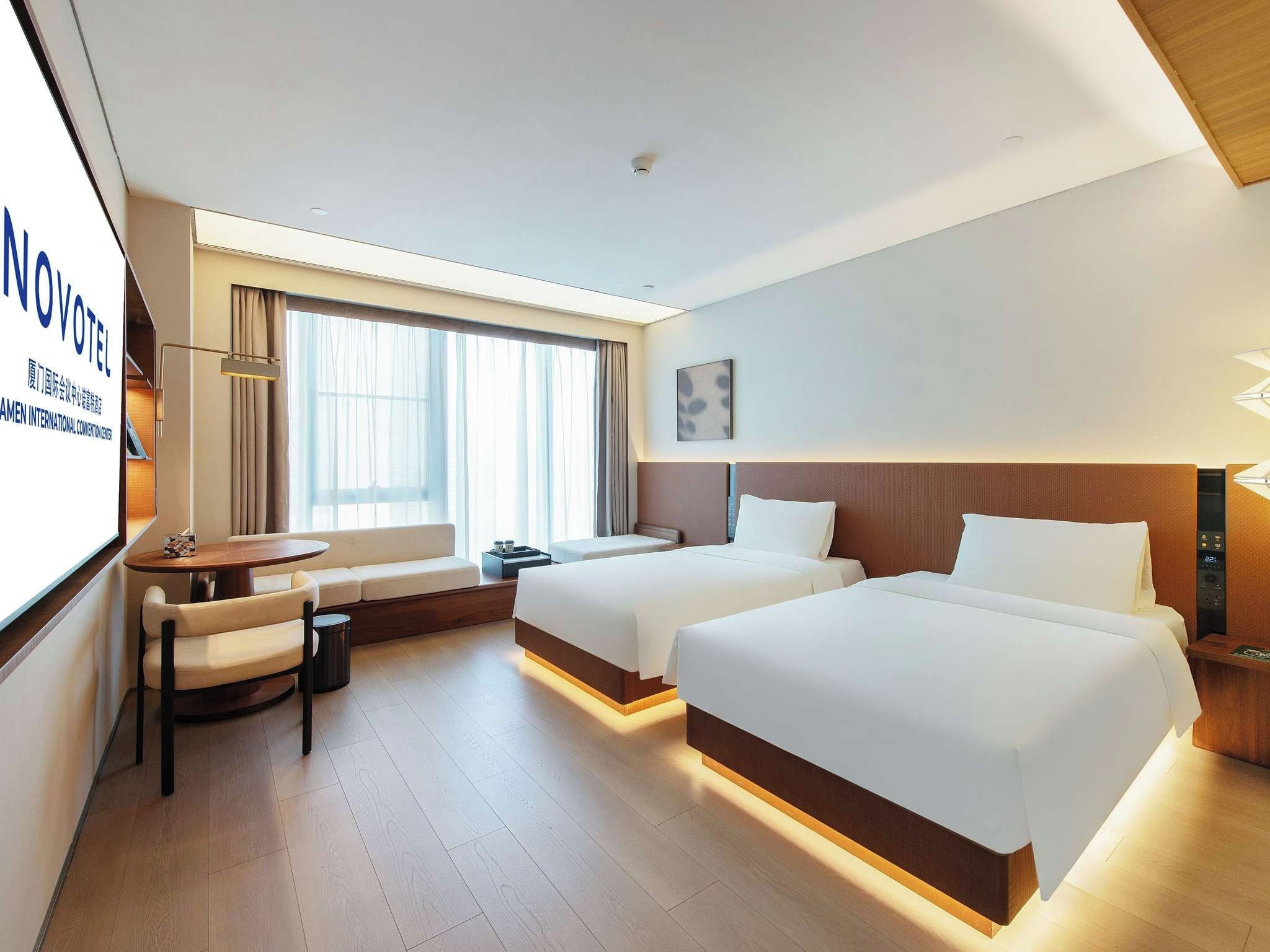 Habitación de hotel con dos camas, un escritorio, una silla y un ventanal grande.