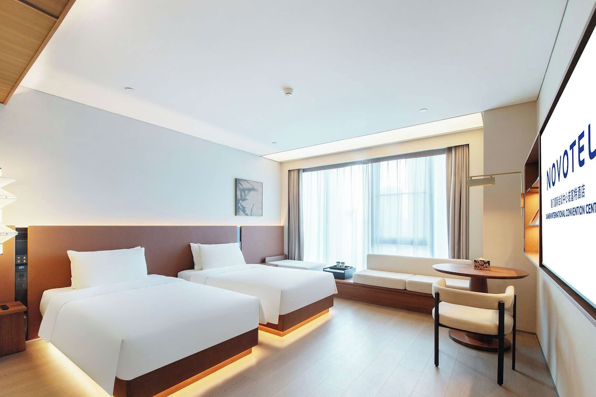 Ein Hotelzimmer mit zwei Betten, einem Schreibtisch und einem großen Fenster.