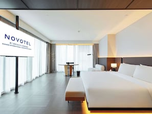 A hotel room with a large bed, a desk, and a chair. There is a sign on the wall that reads "NOVOTEL".