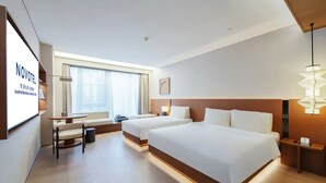 Ein Hotelzimmer mit zwei Betten, einem Schreibtisch, einem Stuhl, einem kleinen Tisch, einer Lampe und einem Fenster mit Vorhängen.