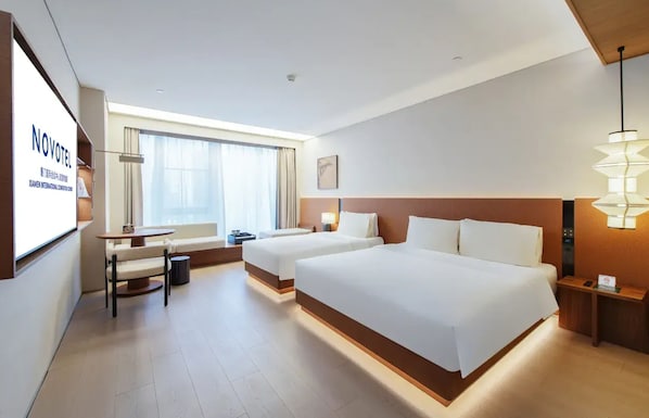 Hotelkamer met twee bedden, een bureau, een stoel, een tafeltje, een lamp en een raam met gordijnen.