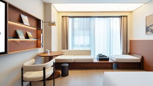 A hotel room with a sofa, a chair, a small table, a trash bin, and a bed. - Novotel Xiamen International Convention Center (Xiamen)