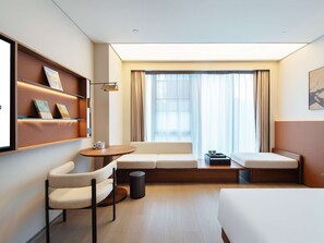 Et hotelværelse med sofa, stol, lille bord, skraldespand og seng.