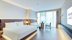 A hotel room with a large bed, a bedside table with a lamp, a small round table with chairs, and a large window with curtains. - Novotel Xiamen International Convention Center (Xiamen)