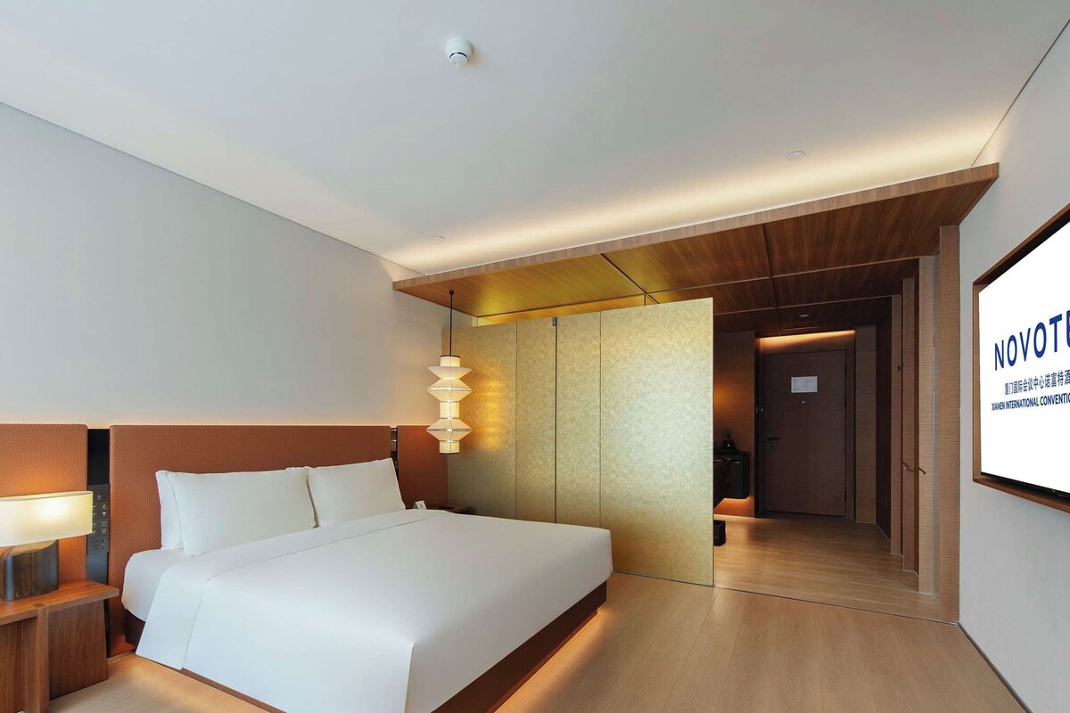 Een moderne hotelkamer met een groot bed, een nachtkastje, een wandlamp en een houten scheidingswand.
