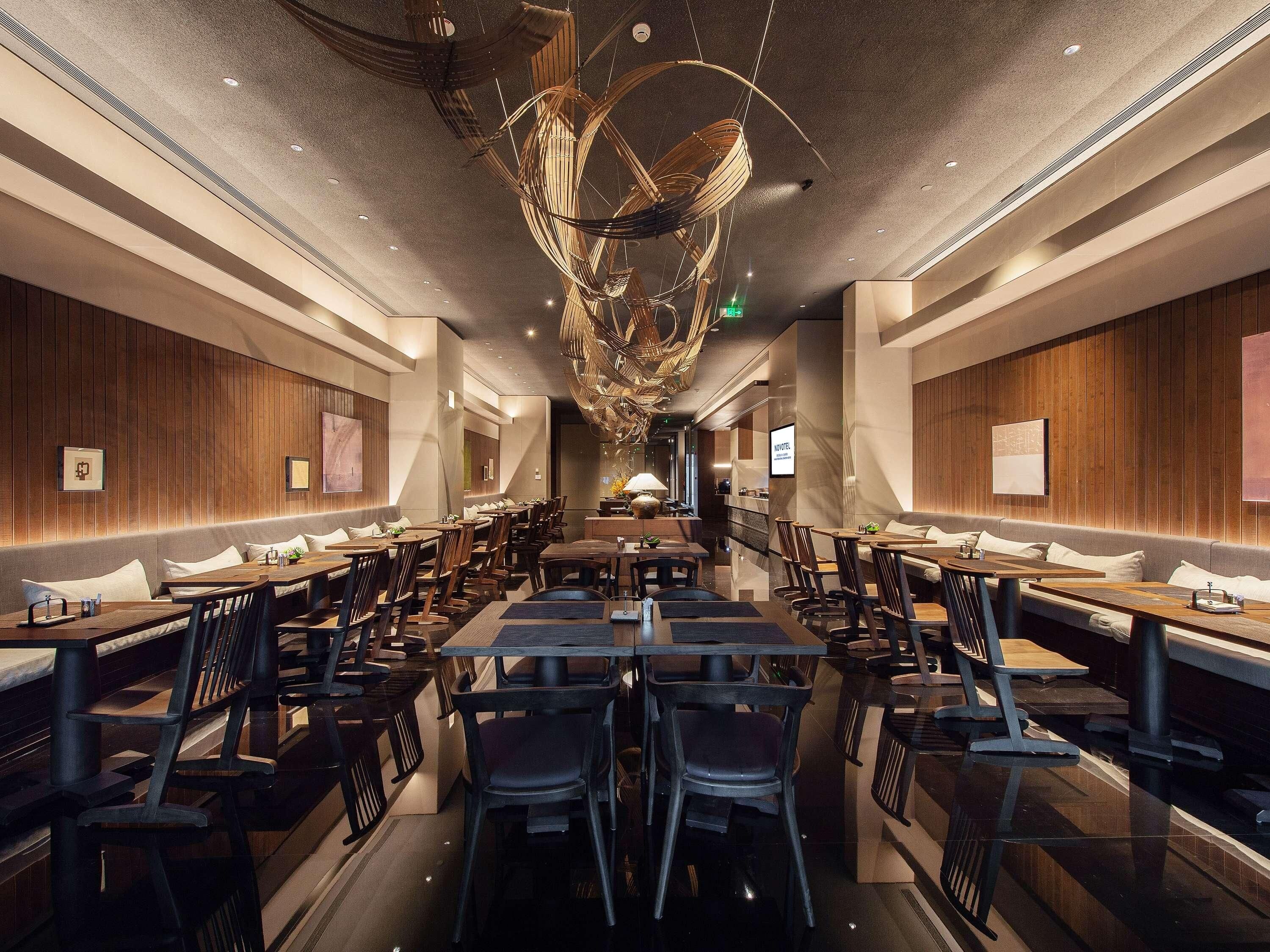 A modern restaurant interior with wooden panel walls, multiple dining tables and chairs, and a unique ceiling light fixture.