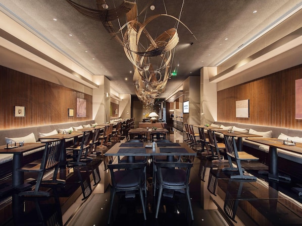Un intérieur de restaurant moderne avec des murs lambrés en bois, de nombreuses tables et chaises, et un luminaire au plafond au design original.
