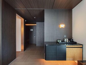 Een modern interieur met een donker houten vloer, een paneelwand in zwart en grijs, en een klein kitchenette met een spoelbak en waterkoker.