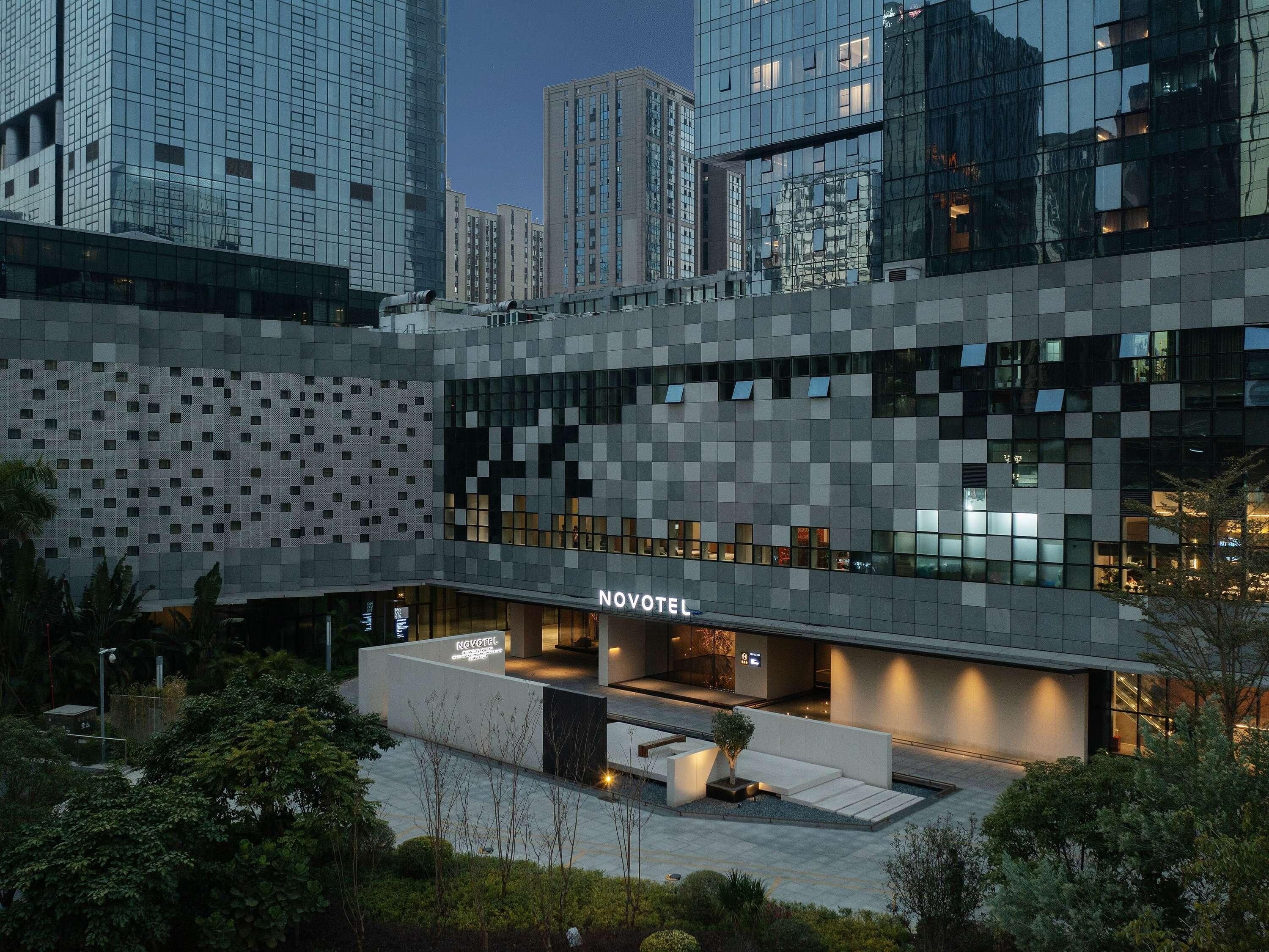A modern hotel with a geometric facade, a well-lit entrance, and a landscaped outdoor area.