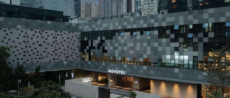 A modern hotel with a geometric facade, a well-lit entrance, and a landscaped outdoor area.