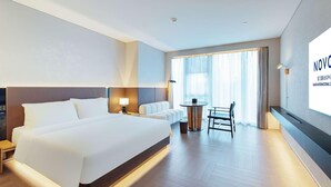 Ein modernes Hotelzimmer mit einem großen Bett, einem kleinen Tisch mit Stühlen und einem großen Fenster mit Vorhängen.