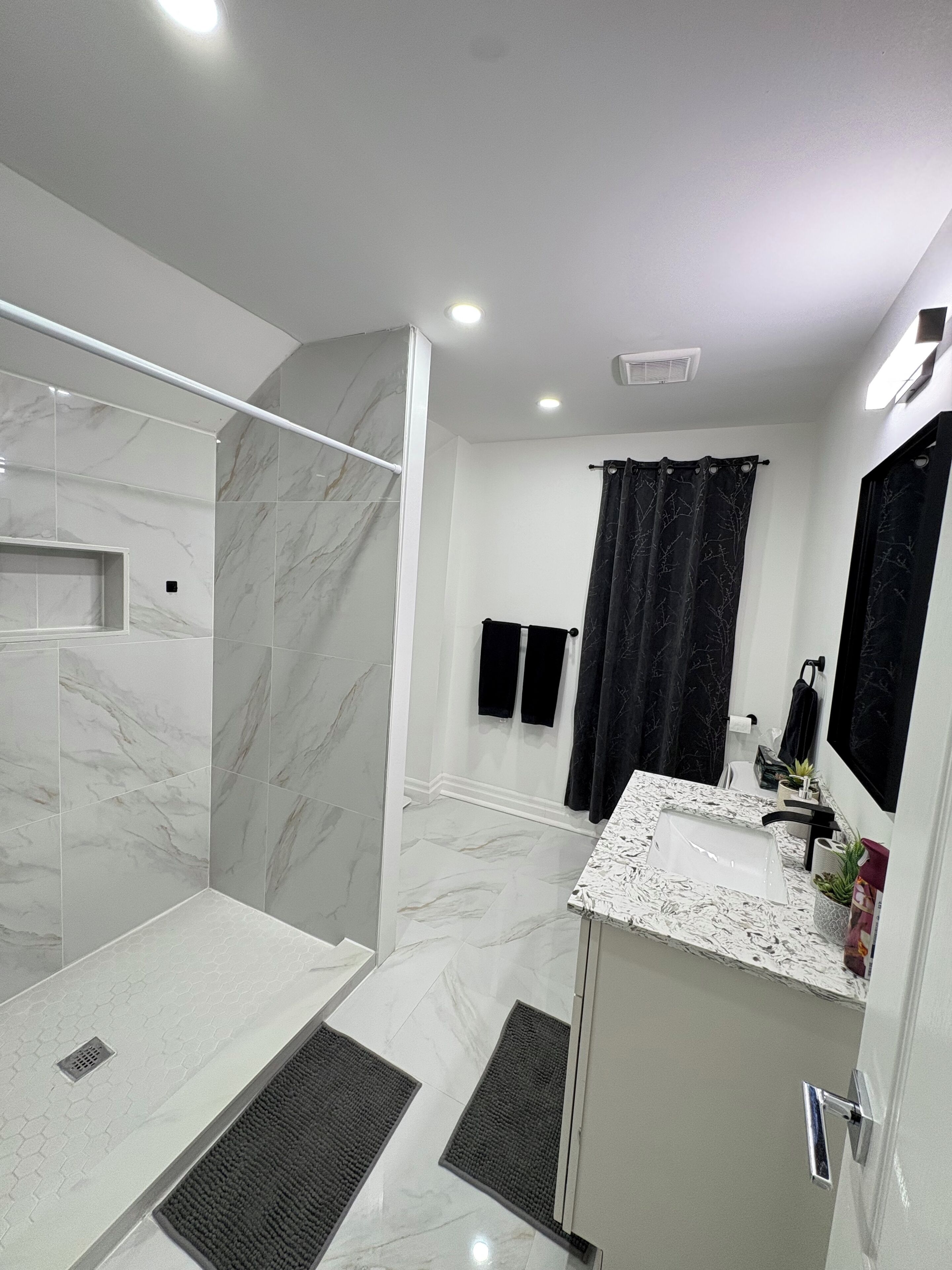 Une salle de bain moderne dotée d’une douche à parois de verre, d’un sol carrelé en marbre, d’un lavabo avec un plan de toilette en marbre et d’un rideau de douche noir.