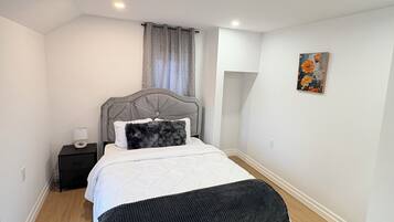 Quarto com cama, mesa de cabeceira, cabeceira, janela com cortinas e uma obra de arte na parede.