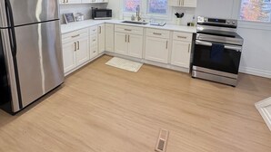 A modern kitchen with white cabinets, stainless steel appliances, and a window providing natural light.