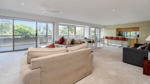 A spacious living area with a large sofa, a dining area with red chairs, and a kitchen with a modern design. - Spacious 2-bed Apartment Near Dining & Attractions (Canberra)