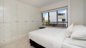 A bedroom with a large wardrobe, a bed with white bedding, and a window with a view of a building. - Spacious 2-bed Apartment Near Dining & Attractions (Canberra)