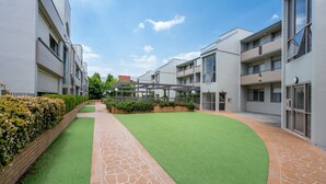 A modern building with a central courtyard, paved walkways, and greenery. - Spacious 2-bed Apartment Near Dining & Attractions (Canberra)