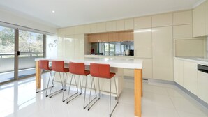 A modern kitchen with a white countertop, beige cabinets, and three orange bar stools. - Spacious 2-bed Apartment Near Dining & Attractions (Canberra)