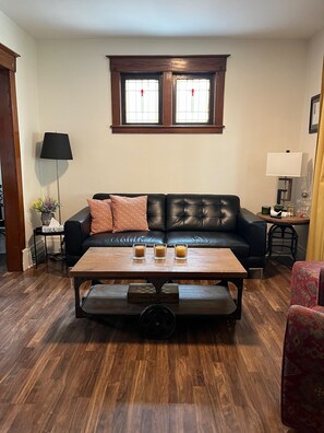 A living room with a black leather sofa, a wooden coffee table, and a window with stained glass. - 3 Bedroom House w/ an Old Charm (Niagara Falls)