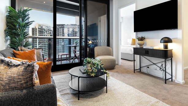 A modern living room with a sofa, coffee table, and a TV mounted on the wall. - Southbank Stay in Prima Tower | Premium Facilities (Southbank)