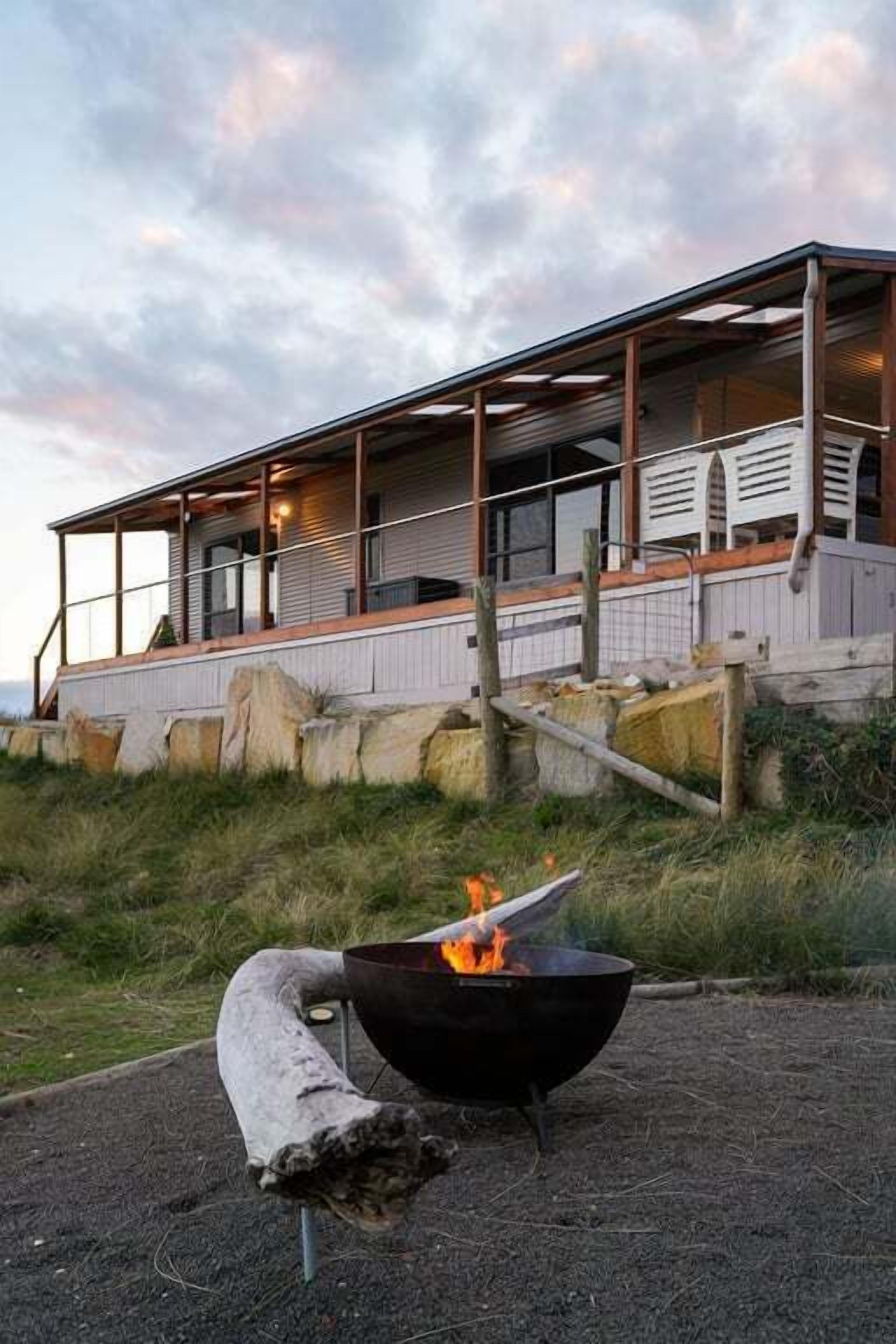 A modern house with a covered porch, a fire pit, and a view of the ocean.