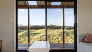A room with a large sliding glass door leading to an outdoor area with a view of a field and distant mountains. - Six-Ten Shores - Holiday Houses Tasmania (Dolphin Sands)