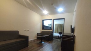 Un espacio habitable compacto con sofá, una mesita redonda, un mueble para televisión y una ventana con cortinas.