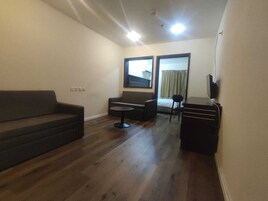 Un espacio habitable compacto con sofá, una mesita redonda, un mueble para televisión y una ventana con cortinas.
