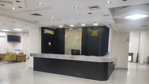 Zona de recepción de hotel con mostrador de mármol, paneles negros y un televisor montado.