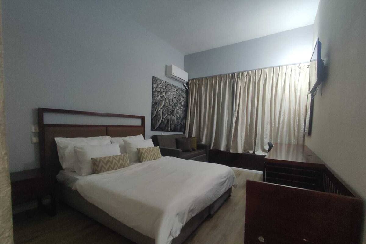 A hotel room with a large bed, a nightstand, a TV mounted on the wall, and a window with curtains.