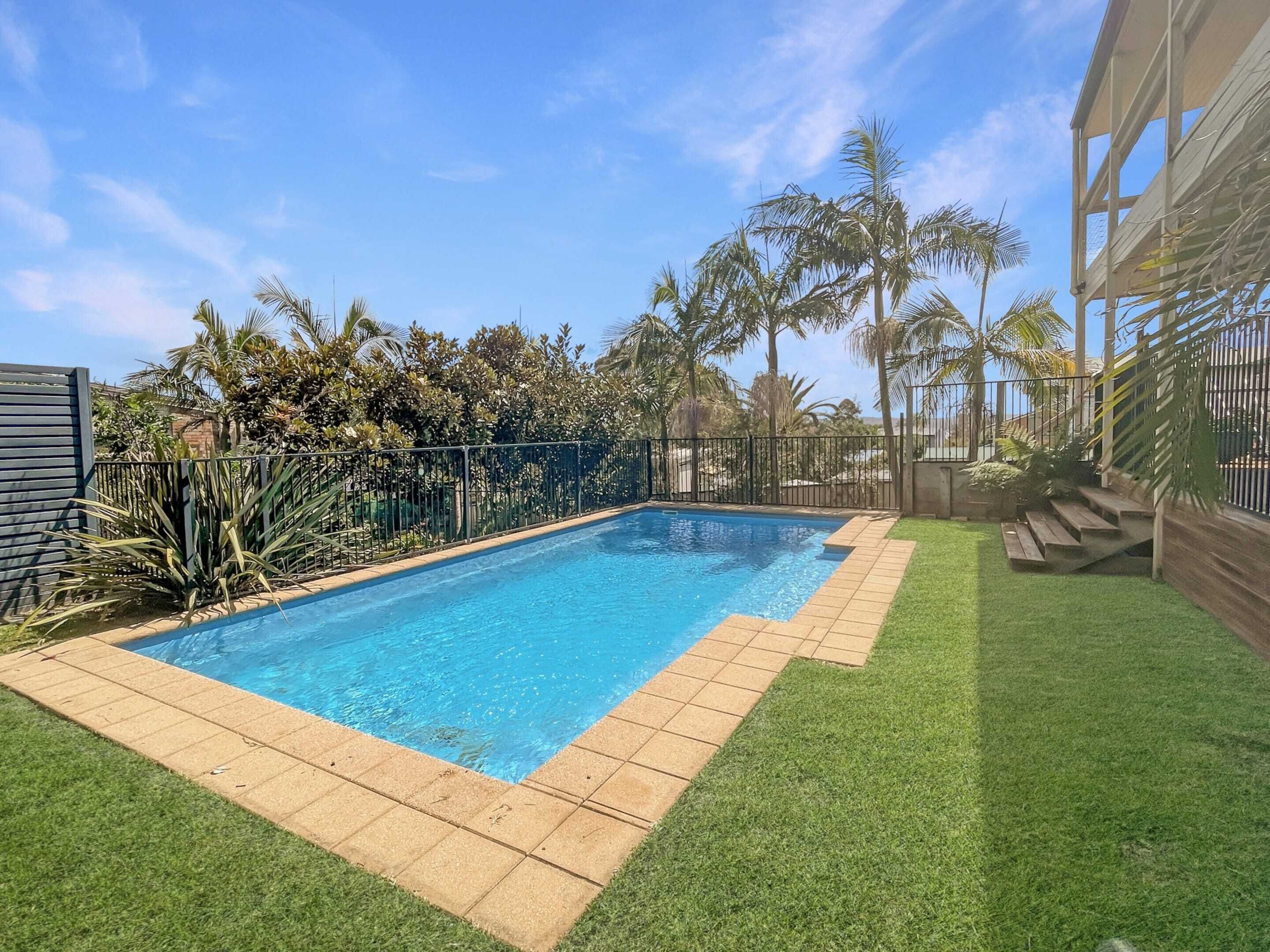 A rectangular swimming pool with a tiled edge, surrounded by a grassy area and a metal fence.