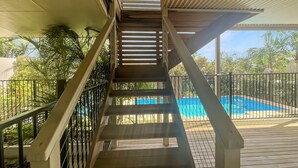 A wooden staircase leading to a pool area with metal railings and a view of palm trees. - Coastal Upper-level Home With Pool Access (Batehaven)