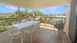 A wooden deck with a table and chairs, overlooking a scenic view of a coastline and greenery. - Coastal Upper-level Home With Pool Access (Batehaven)