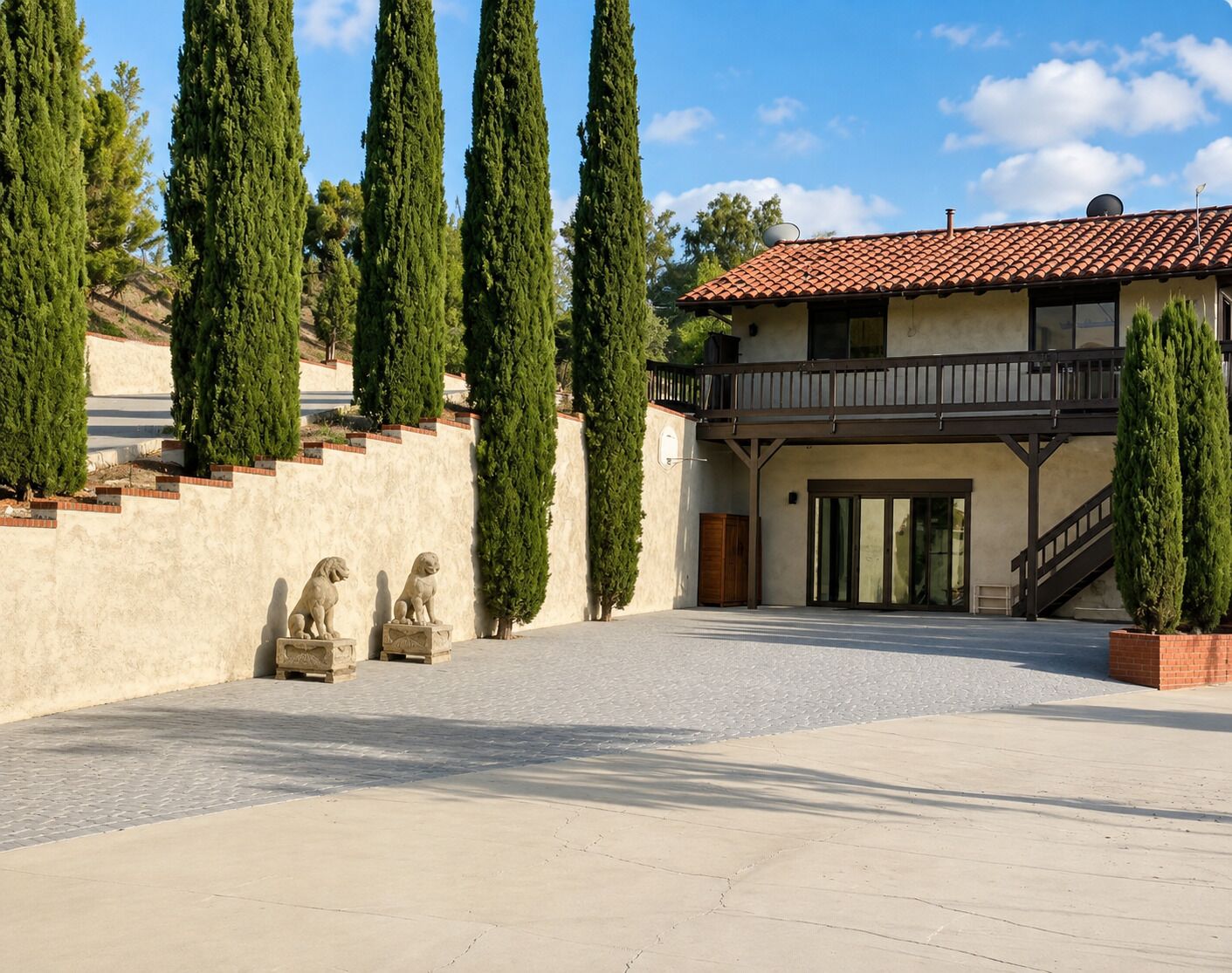 A building with a tiled roof, a balcony, and a paved courtyard with statues.