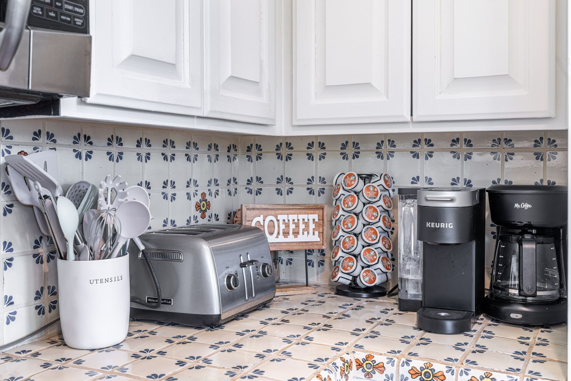 A kitchen with white cabinets, a toaster, a coffee maker, and a coffee-themed wall decoration.
