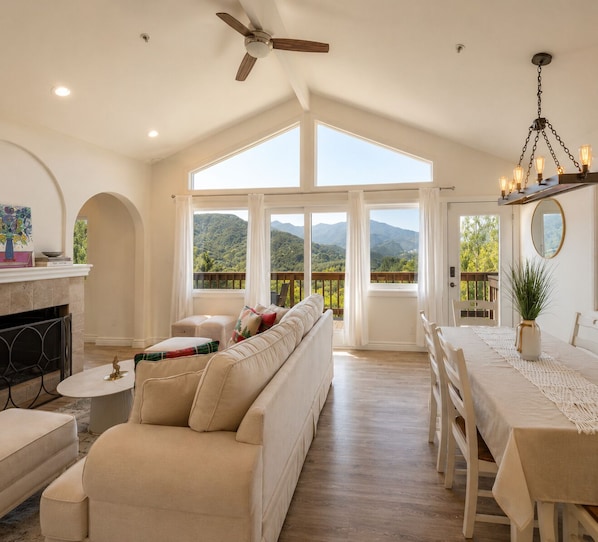 A spacious living room with a fireplace, a sofa, and a dining area with a view of the mountains.