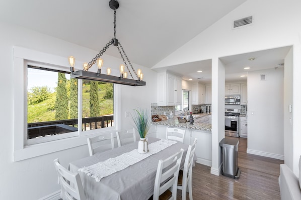 Una cocina moderna con armarios blancos, una campana extractora de acero inoxidable y un amplio ventanal con vistas a la vegetación.