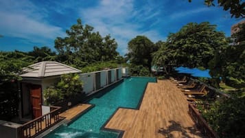 A swimming pool with a wooden deck, surrounded by lush greenery and trees.