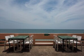 Una terrassa amb taules i caires, una banca i vista al mar.