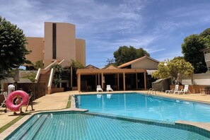 A swimming pool with a tiled deck, lounge chairs, and a building in the background. - Sailom Hotel Hua Hin (Hua Hin)
