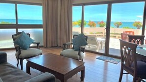 Ein Zimmer mit großem Fenster, einem Holztisch, zwei Sesseln und einem Sofa.