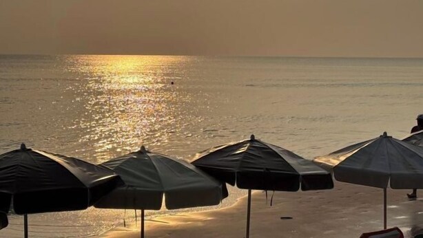 Ein Strand mit Sonnenschirmen und einem Sonnenuntergang über dem Wasser.
