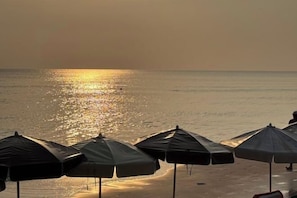 Une plage avec des parasols et un coucher de soleil sur l’eau.