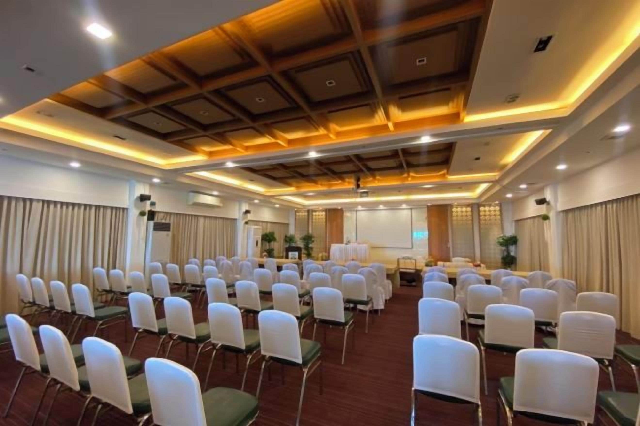 A conference room with rows of white chairs, a wooden ceiling, and a projector screen.