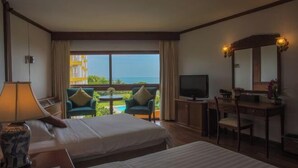 Ein Hotelzimmer mit zwei Betten, einem Schreibtisch, einem Sessel, einem Fernseher und einem Balkon mit Meerblick.