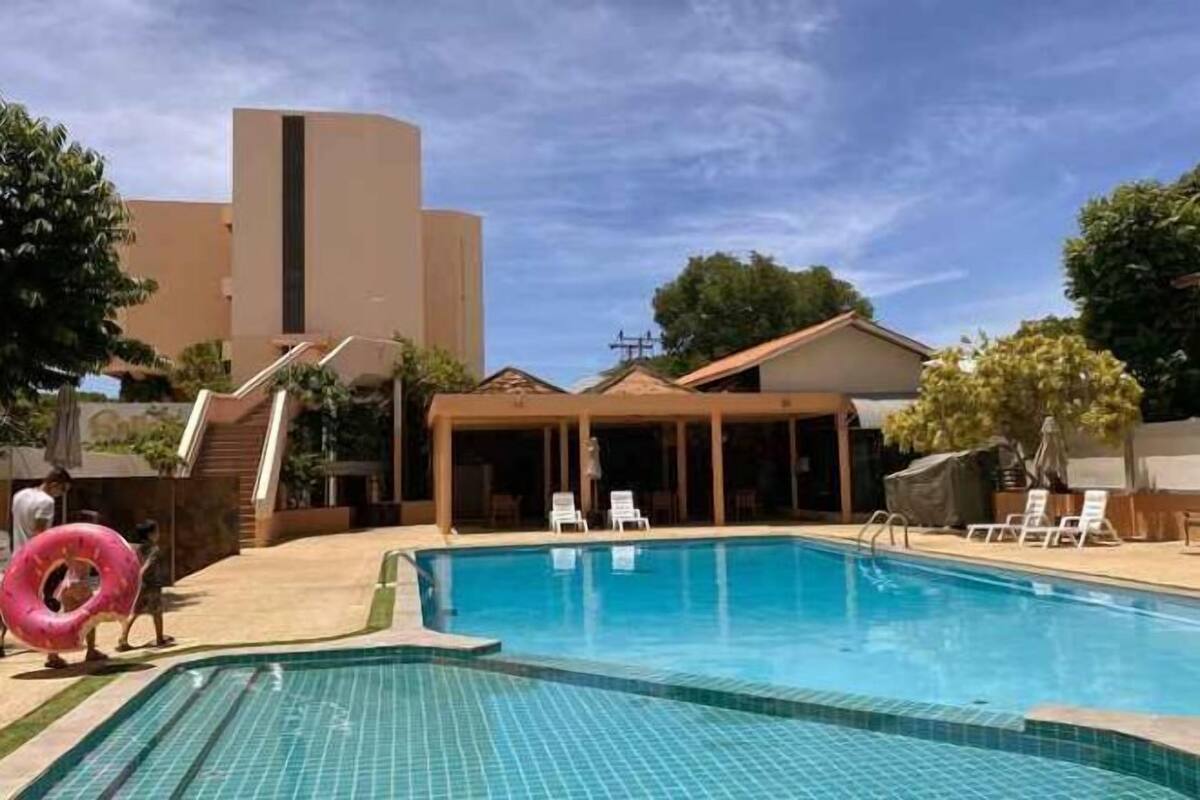Una piscina con lettini, una zona ombreggiata e un edificio sullo sfondo.