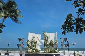 Une cérémonie de mariage organisée sur la plage, avec une scène, des décorations florales et une vue dégagée sur l’océan.