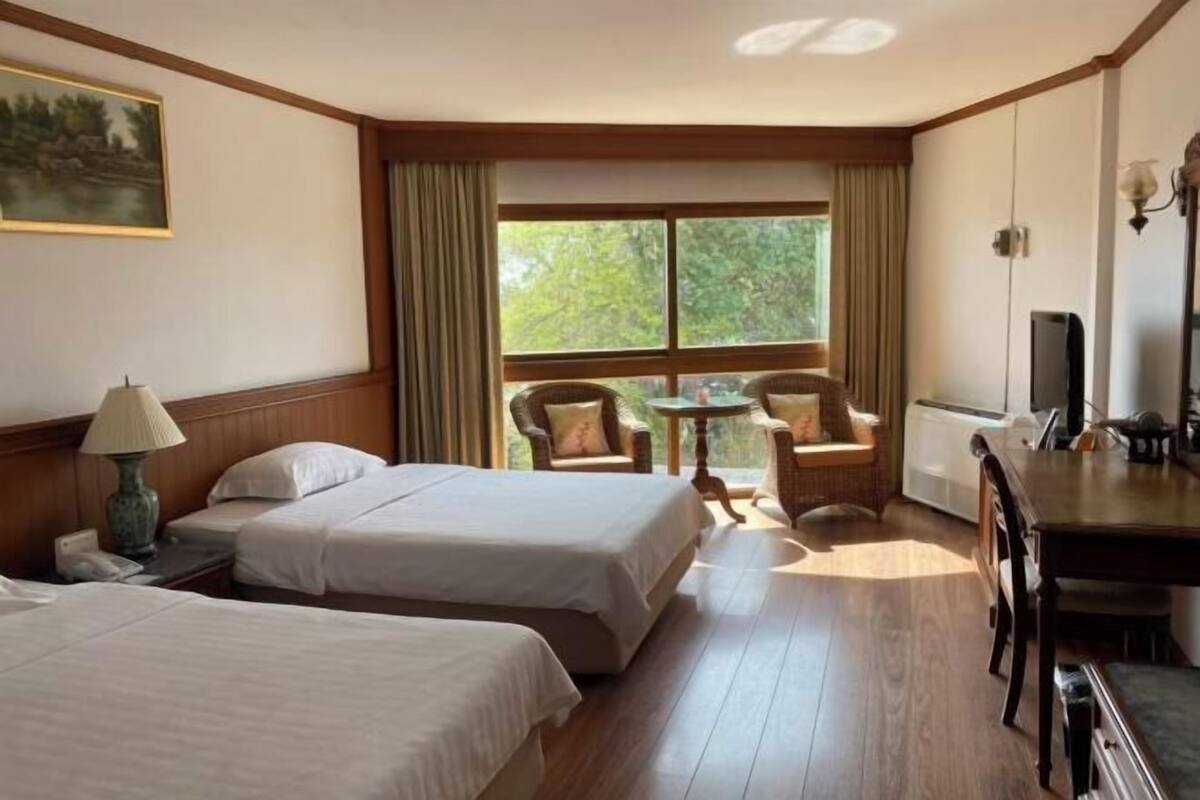 Una camera d'albergo con due letti, un tavolo da pranzo, una televisione e una finestra con tende.